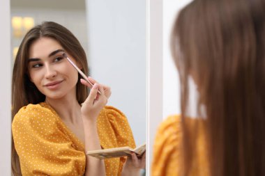 Güzel bir kadın aynanın yanında göz farı sürüyor.