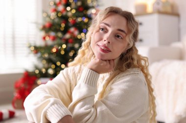 Evdeki bulanık ışıklara karşı süveterli, gülümseyen kadın. Mutlu Noeller ve mutlu yıllar.