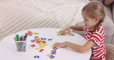 Beyaz masada harflerle alfabe öğrenen küçük bir kız.