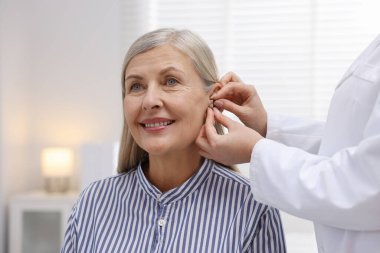 Doktor klinikte hastanın kulağına işitme cihazı takıyor.