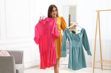 Kadın içeride pembe ve mavi elbiseler arasında seçim yapıyor.