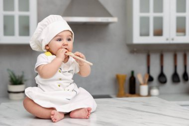 Mutfaktaki açık mermer masada spatulalı şirin bir bebek şef üniforması giyiyor. Metin için boşluk