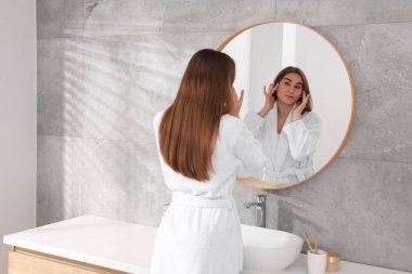 İçerideki aynanın yanında bornozlu güzel bir kadın.