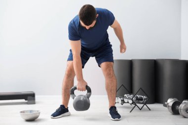 Spor salonunda kettlebell ile egzersiz yapan güçlü bir adam.