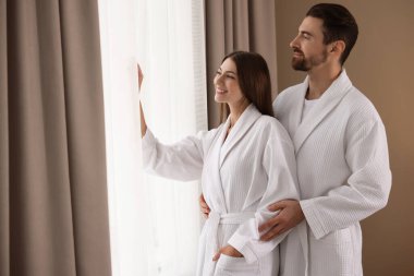 Otel odasının penceresinin yanında bornoz giyen mutlu çift.