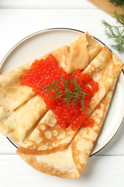 Kırmızı havyarlı leziz krepler ve beyaz ahşap masadaki dereotlar.