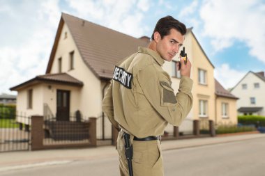 Üniformalı güvenlik görevlisi evin yakınında telsiz kullanıyor. Özel mülk koruması