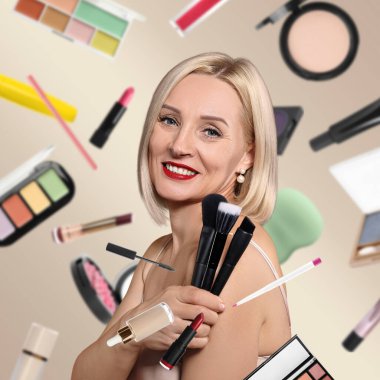 Bej arka planda fırçaları olan güzel bir kadın. Farklı dekoratif kozmetik ürünleri makyaj sanatçılarının etrafında düşüyor.