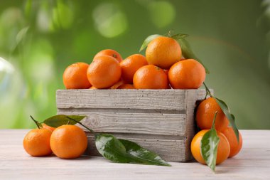 Taze, sulu mandalinalar beyaz ahşap masada, bulanık yeşil arka planda.