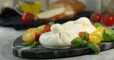 Açık gri masada nefis burrata peyniri ve domateslere fesleğen koyan kadın, yakın plan.