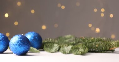 Kadın, bulanık ışıklara karşı beyaz masaya Noel süsü ve hediye koyuyor.