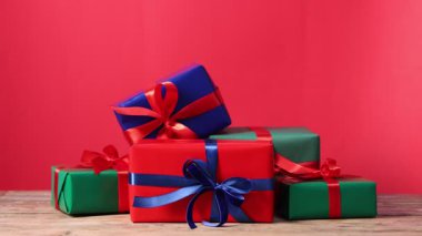 Kadın, kırmızı arka plana karşı ahşap masaya hediye kutusu koyuyor, yakın plan. Mutlu Noeller ve mutlu yıllar.