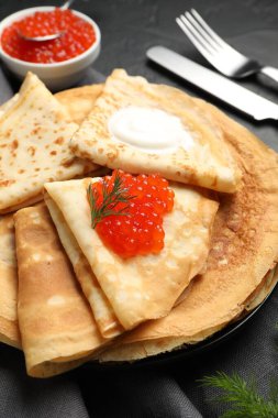 Kırmızı havyarlı leziz krepler ve siyah masada ekşi krema, yakın plan.