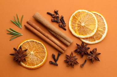 Farklı baharatlar, taze biberiye ve turuncu arka planda sıcak şarap için kuru narenciye dilimleri.