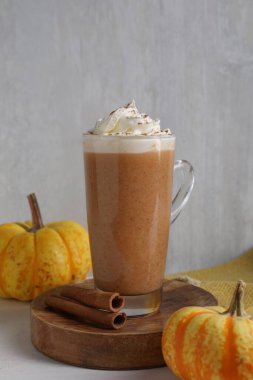 Krem şantili balkabaklı latte, tarçın çubukları ve gri duvarın yanındaki beyaz masada taze sebzeler, yakın plan.