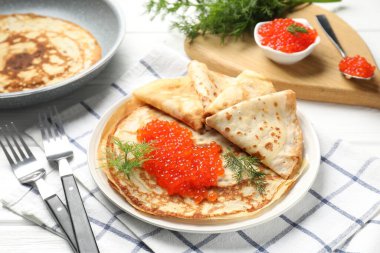 Beyaz ahşap masada servis edilen kırmızı havyarlı leziz krepler.