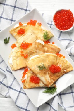 Kırmızı havyarlı leziz krepler ve beyaz ahşap masaya ekşi krema.