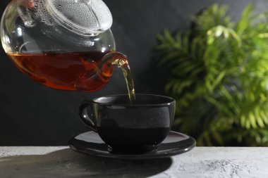 Gri masada çaydanlıktan fincana sıcak çay dolduran kadın, yakın plan. Metin için boşluk