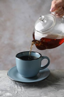 Gri masadaki çaydanlıktan fincana sıcak çay dolduran kadın, yakın plan.