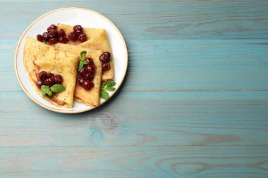 Açık mavi ahşap masada vişne reçeli ile servis edilen leziz krepler, üst manzara. Metin için boşluk