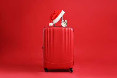 Noel tatili. Kırmızı arka planda Noel Baba şapkası ve alarmlı çanta.