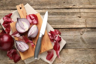 Fresh onion bulbs with peels and knife on wooden table, flat lay. Space for text