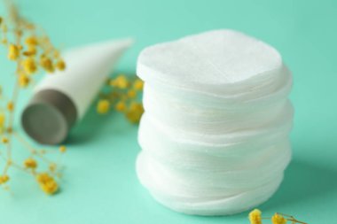 Turkuaz arka planda bir yığın temiz pamuk pedi, krema ve çiçek, yakın plan.