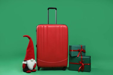 Noel tatili. Zarif bavul, hediye kutuları ve yeşil arka planda dekoratif cüce.