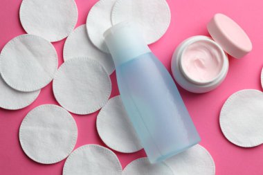 Pembe arka planda temiz pamuk pedleri ve kozmetik ürünleri, düz yatıyordu.