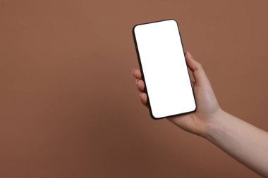 Kahverengi arka planda boş ekranlı akıllı telefonu olan bir kadın, yakın plan. Tasarım için model
