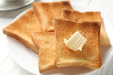 Beyaz ahşap masada tereyağlı taze kızarmış ekmek dilimleri, yakın plan.