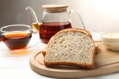 Beyaz ahşap masada tereyağı ve çay ile ekmek dilimleri, yakın plan.