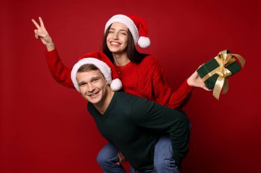 Kırmızı arka planda Noel Baba şapkalı mutlu çift