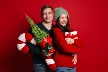 Mutlu çift Noel hediyesiyle, thuja ağacı ve kırmızı arka planda dekoratif şeker kamışı.