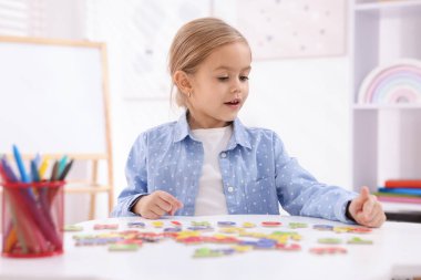 Beyaz masada harflerle alfabe öğrenen küçük bir kız.