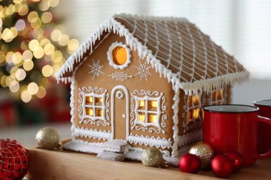 Güzel zencefilli kurabiye evi, kapalı alanda bulanık ışıklara karşı tepside fincanlar ve takılar, yakın çekim. Noel atmosferi