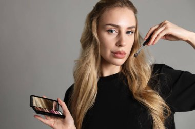 Göz farı paleti ve açık gri arka planda fırçası olan makyaj sanatçısı