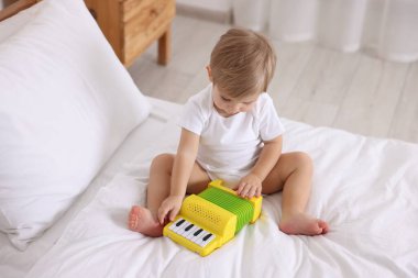 Evdeki yatakta oyuncak akordeonla oynayan sevimli küçük çocuk.