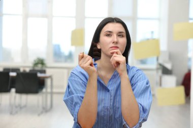 Ofisinde yapışkan notlar olan cam tahtanın yanındaki kadın.