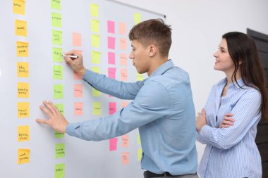 Meslektaşlar, ofiste yapışkan notlarla beyaz tahtaya yakın stratejileri tartışıyor