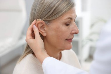 Doktor klinikte hastanın kulağına işitme cihazı takıyor.