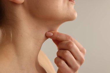 Açık gri arka planda boynuna dokunan kadın, yakın plan. Metin için boşluk