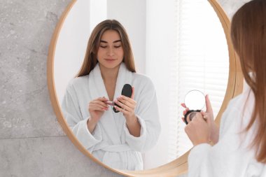 Bornozlu güzel bir kadın aynanın yanında makyaj yapıyor.