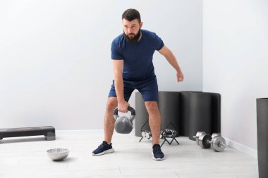 Spor salonunda kettlebell ile egzersiz yapan güçlü bir adam.