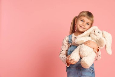 Tulum giymiş, pembe arka planda oyuncak tavşanla gülümseyen küçük bir kız. Metin için boşluk