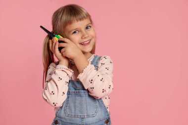 Pembe arka planda radyo kullanan tulumlu mutlu küçük kız. Metin için boşluk