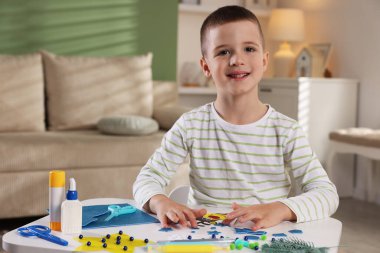 Küçük çocuk kapalı bir masada Noel kartı hazırlıyor. Çocuk el yapımı.