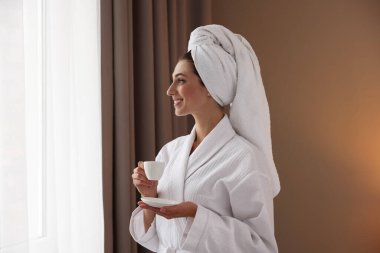 Bornozlu güzel bir kadın, sarılmış saçlarıyla sabah kahvesini evin içinde içiyor.