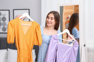 Kadın içeride menekşe ve turuncu elbiseler arasında seçim yapıyor.