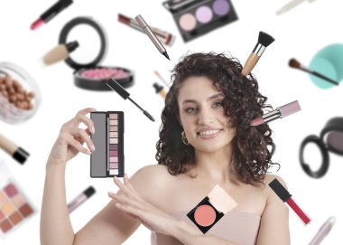 Beyaz arka planda göz farı paleti olan güzel bir kadın. Farklı dekoratif kozmetik ürünleri makyaj sanatçılarının etrafında düşüyor.